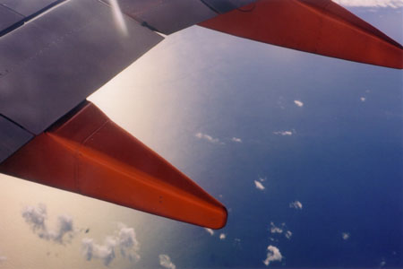 Dramatic red of the plane's wing contrasted to the white and blue of clouds and sea.